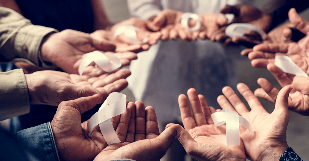 group of hands holding white ribbons for cancer support