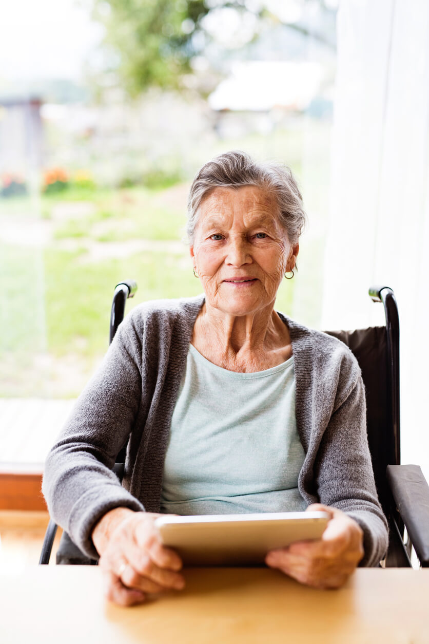 Image of an older woman in a wheelchair sitting at a table and holding an ipad