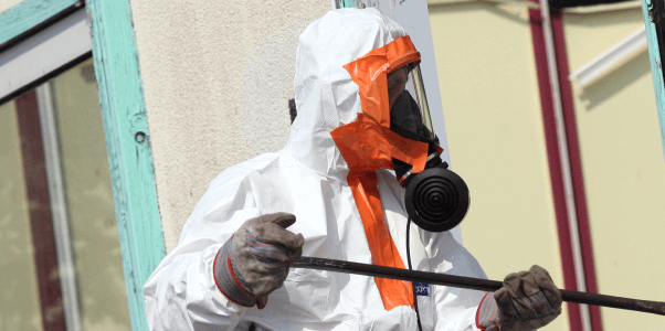 Photograph of someone in a white and orange hazmat suit holding a black rod.