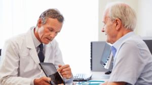 A doctor points to an ipad while speaking to an older male patient