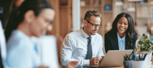 A male lawyer sits at a laptop while a female lawyer looks over his shoulder at his screen