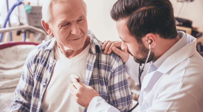 A doctor holds up a stethoscope to the chest of an older male patient