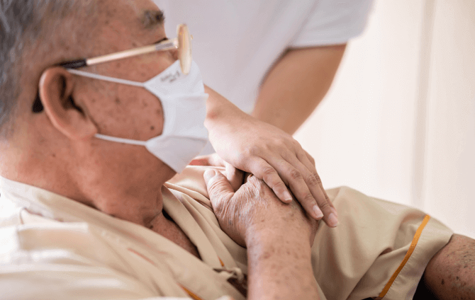 an older patient holds the hands of another person who is partially off-camera