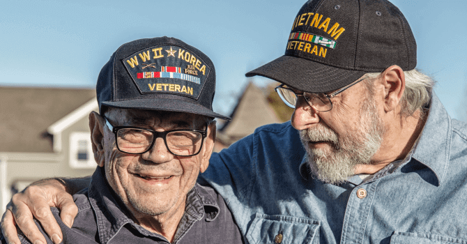 An elderly vietnam veteran puts his hand on the shoulder on a veteran who served in both World War II and Korea
