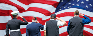 a group of veterans (with their back to the viewer) salutes a large American flag