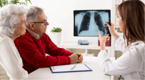 A mesothelioma doctor points at a lung X-ray while a husband and wife observe.