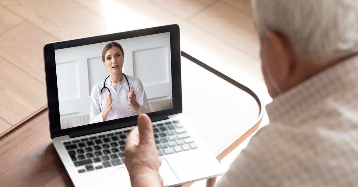 An older person sits on a laptop and listens to a nurse via a teladoc appointment