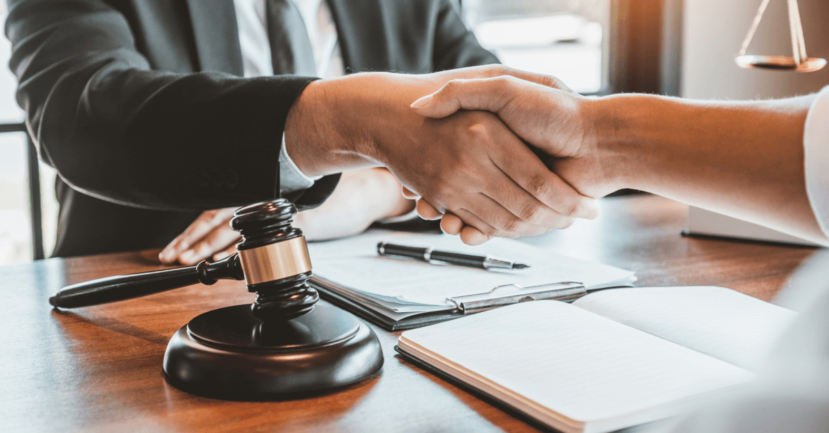a lawyer shakes the hand of another person sitting across from them at a desk