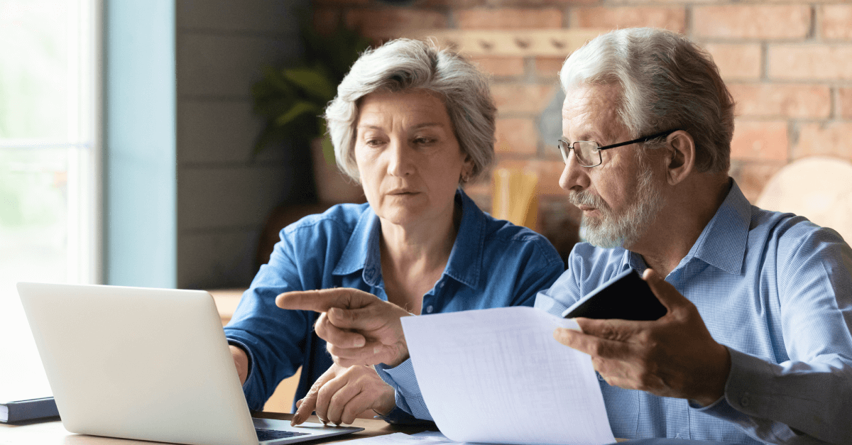 an older couple looks at documents and a computer screen