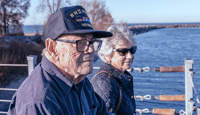 An older veteran walks with an older woman on a bridge over a body of water
