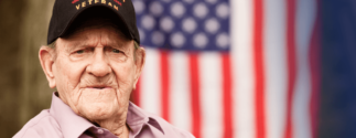 An older World War II veteran sits down. An American flag is in the background.