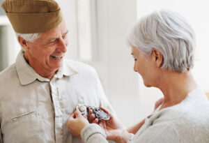 an older woman looking at her husbands medals as he stands wearing his full army uniform