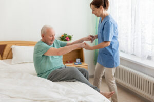 A home health aide helps an elderly male patient get out of bed