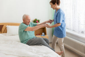 A home health aide helps an older male patient get out of bed