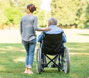 A woman stands with her hand on the shoulder of an older man in a wheelchair