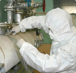 A person in a white hazardous materials suit works on a boiler