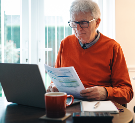 An older man in a red shirt looks at documents in his hands