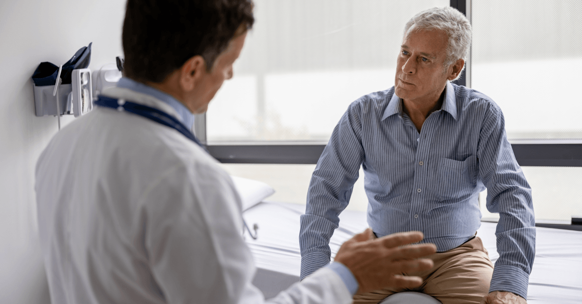 An older man sits with a younger male doctor
