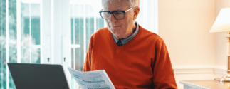 An older man in a red shirt looks at documents in his hands