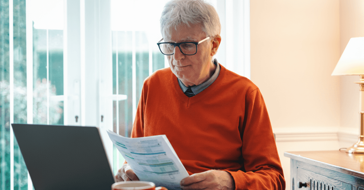 An older man in a red shirt looks at documents in his hands