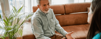 An older man sits on a couch while a younger woman approaches